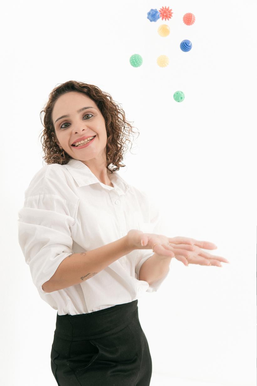 Thais lançando bolinhas sensoriais coloridas para o alto, sorrindo
