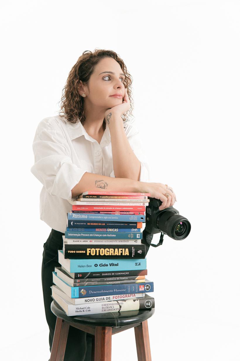 Thais de Sá apoiada numa pilha de livros de desenvolvimento infantil e fotografia, com a câmera ao lado